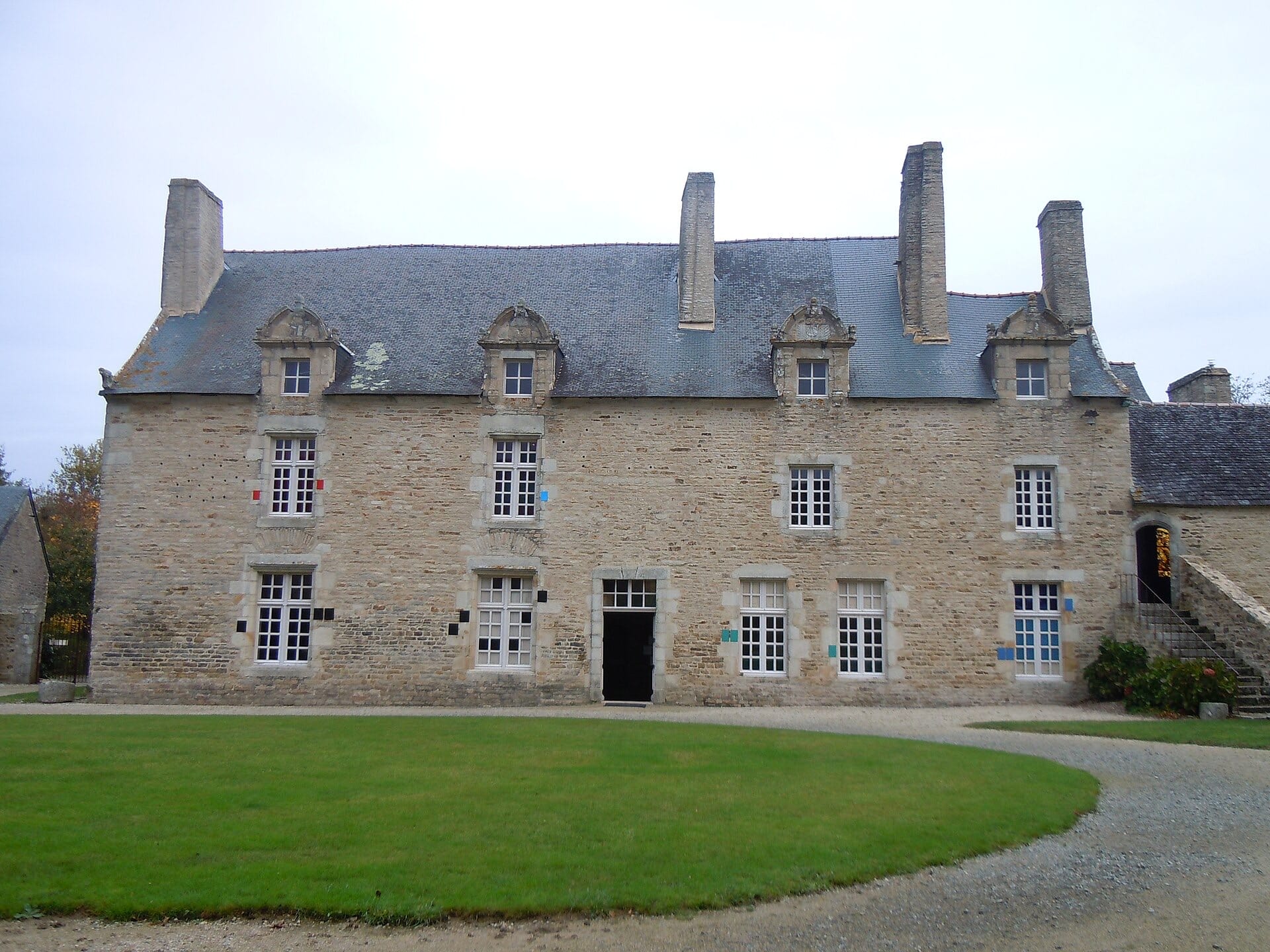 Façade de manoir breton en moellons de granit à chaînages de pierre, hautes souches de cheminée, lucarnes à fronton, toit d’ardoise