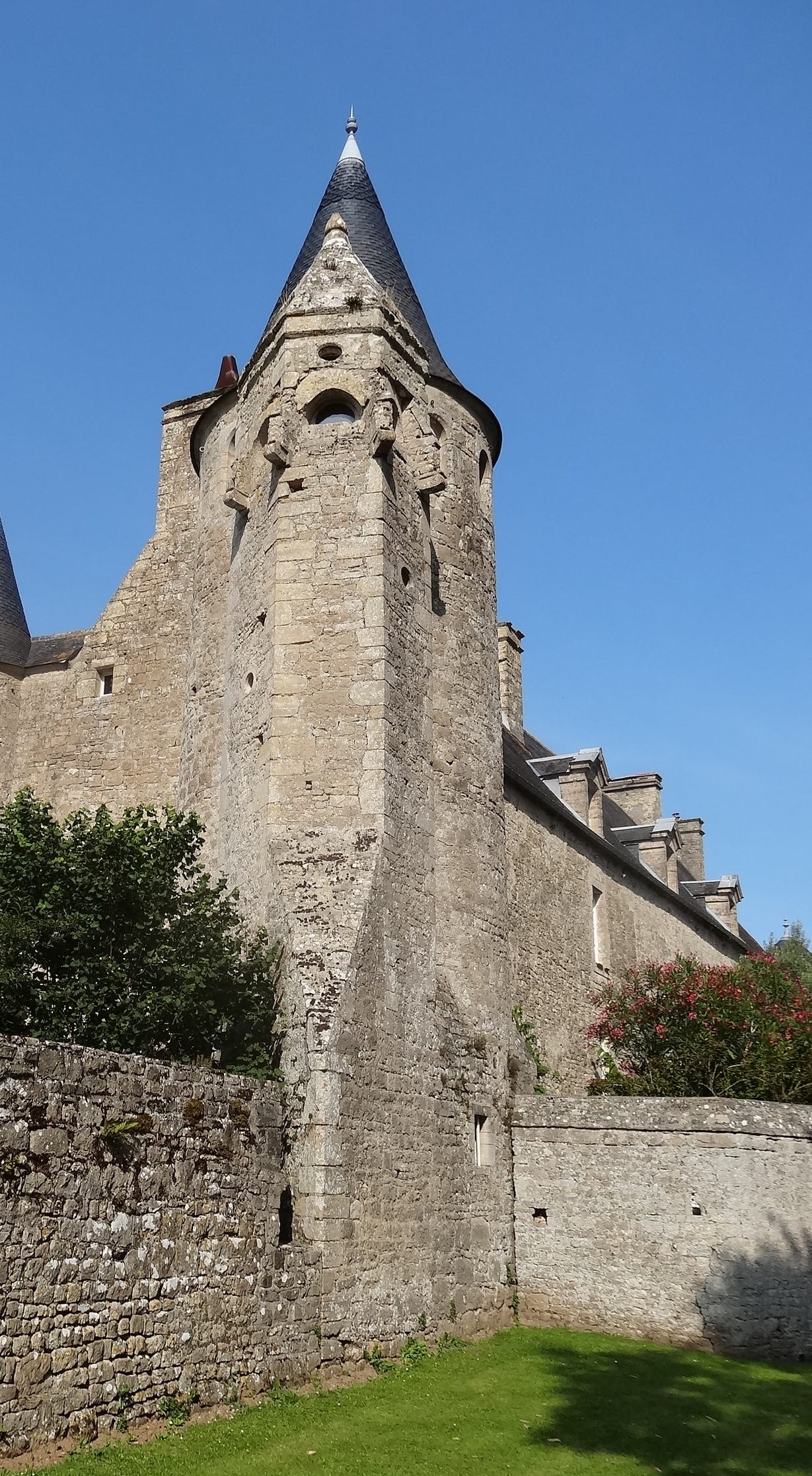 Haute tour d’escalier polygonale en encorbellement sur base talutée, coiffée d’un toit conique d’ardoise, accolée au logis de pierre