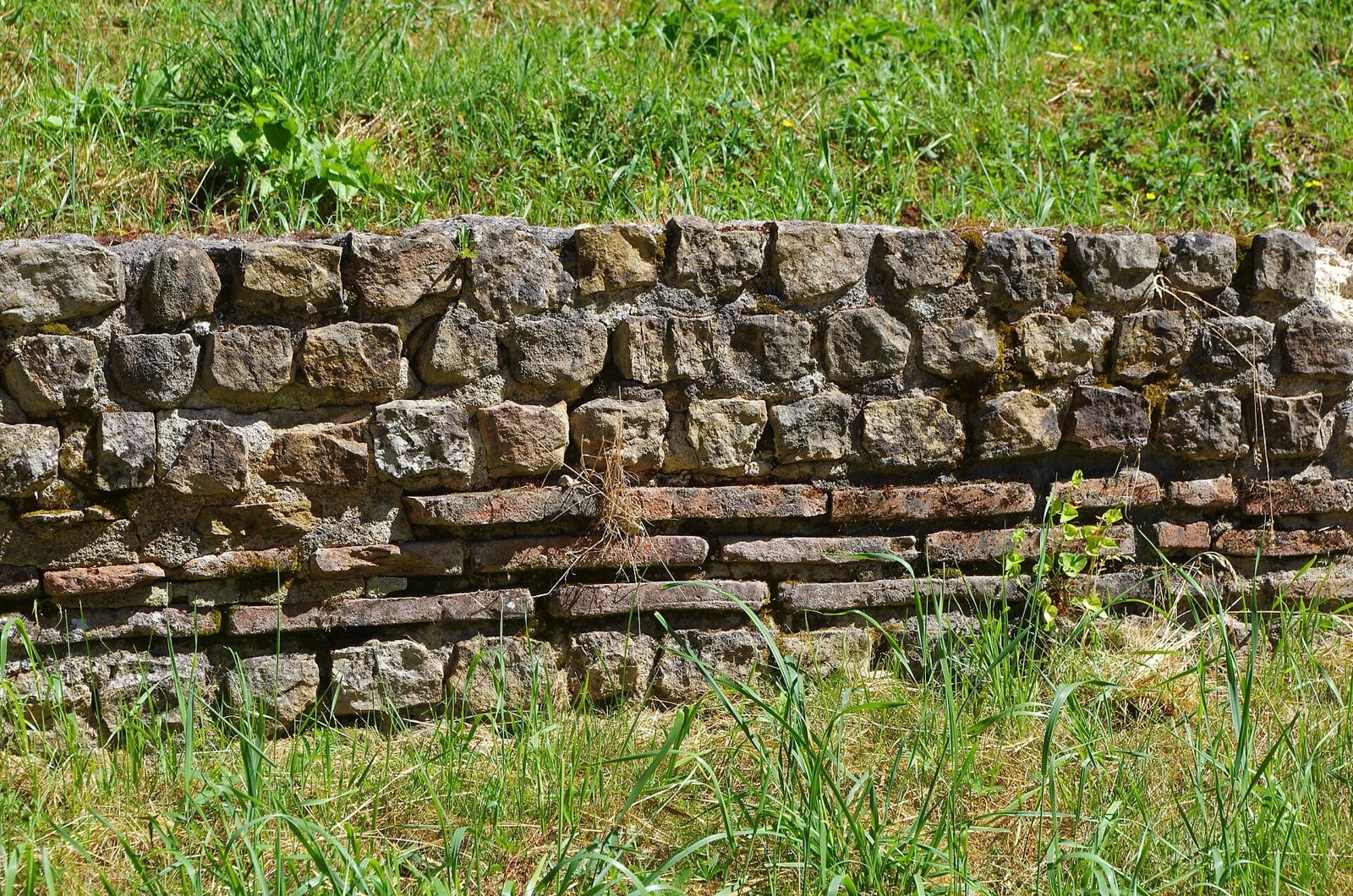 Mur ancien de moellons calcaires irréguliers réglés de minces lits de brique, aux joints débordants
