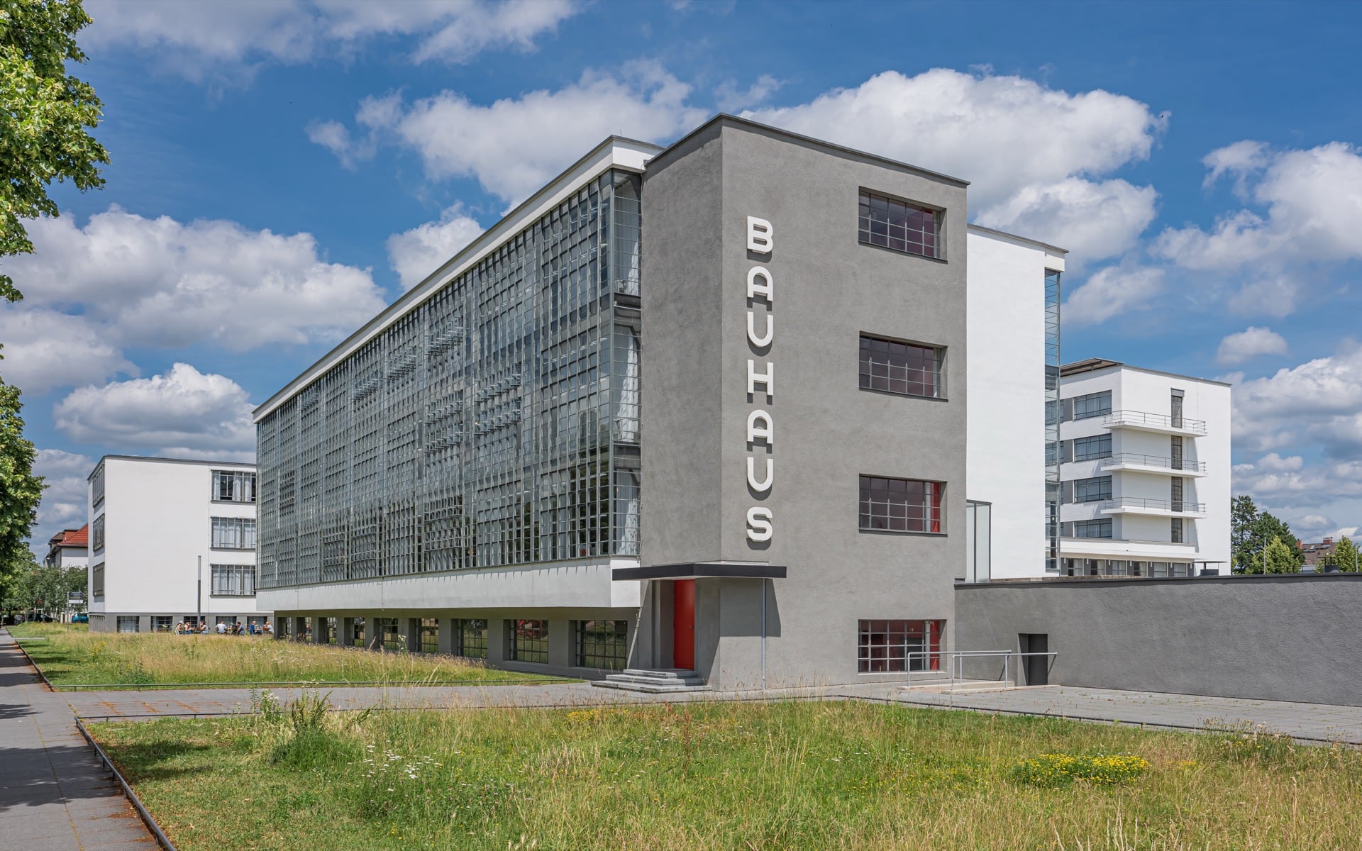 Le bâtiment du Bauhaus à Dessau : grand mur-rideau de verre et volumes blancs et gris, portant « Bauhaus » en lettres verticales, sous un ciel bleu
