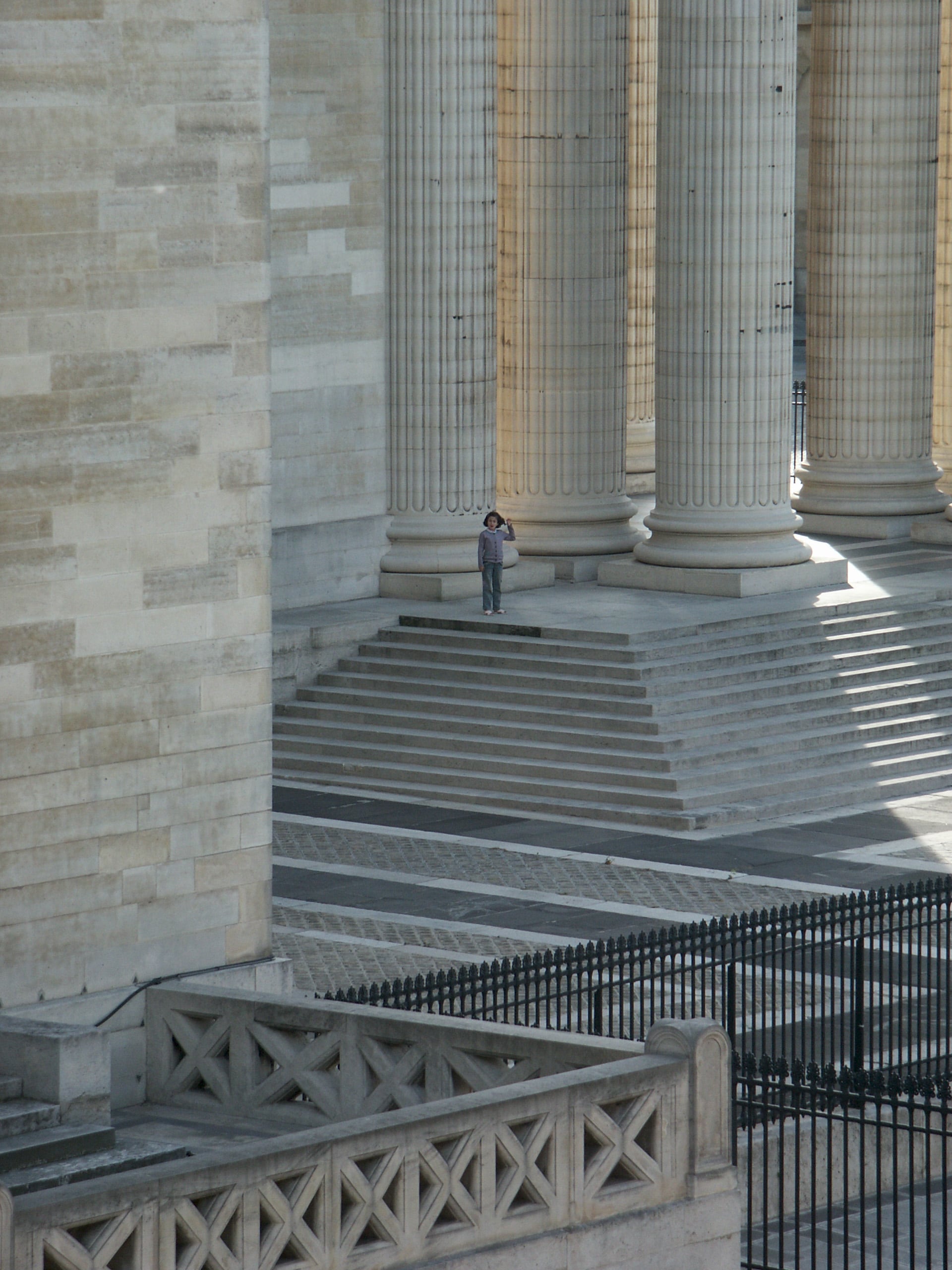 Les colonnes corinthiennes cannelées du portique du Panthéon de Paris, vues depuis les marches, un enfant au pied donnant l’échelle