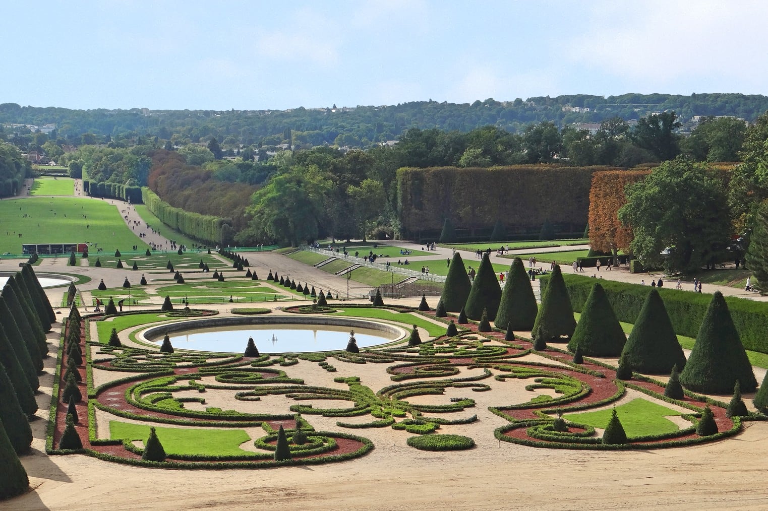Vue plongeante sur le grand parterre du domaine de Sceaux : arabesques de buis taillé sur fond de terre rouge, autour d’un bassin circulaire, encadrées d’ifs taillés en cônes, dans l’axe de la perspective descendante.