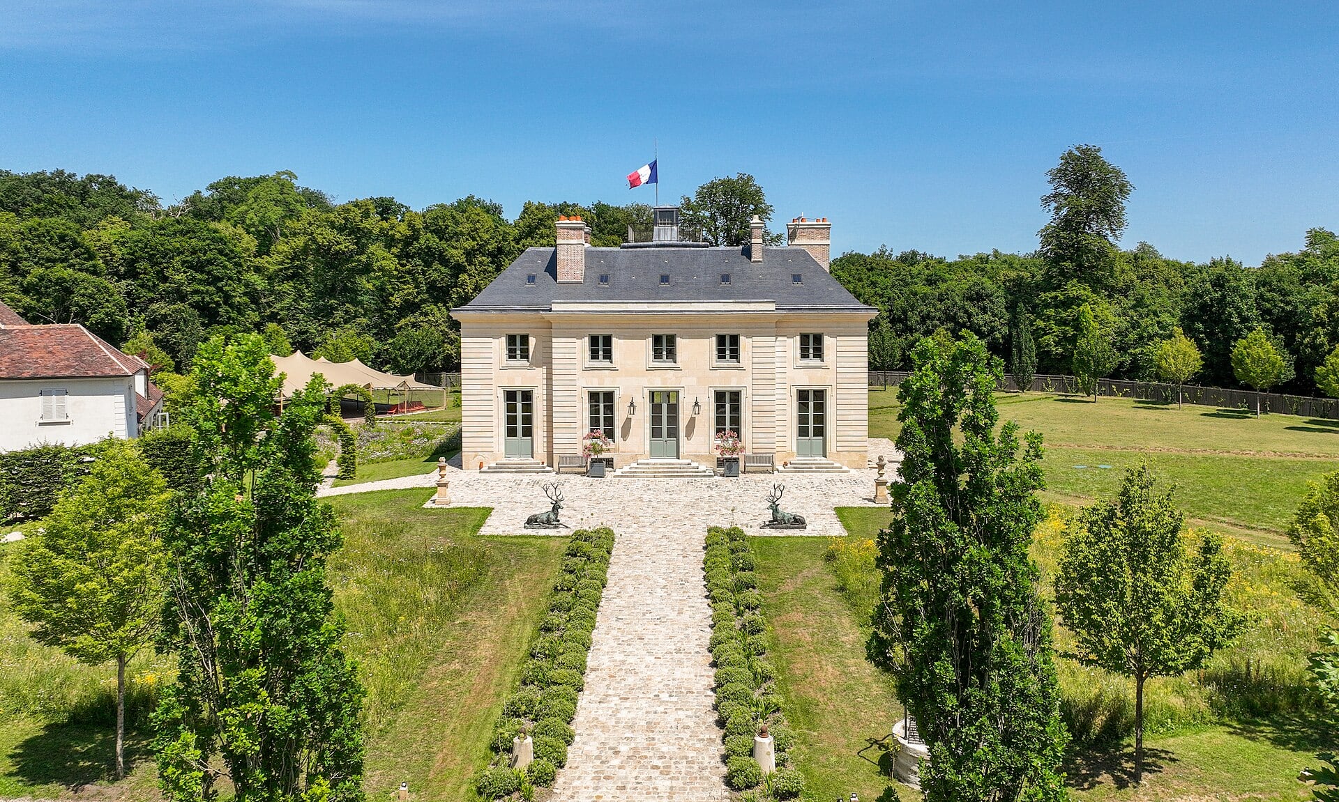 Vue aérienne de la façade principale du pavillon de la Muette à Saint-Germain-en-Laye, bâtiment symétrique en brique et pierre precede d’une allée bordée de statues de cerfs en bronze.