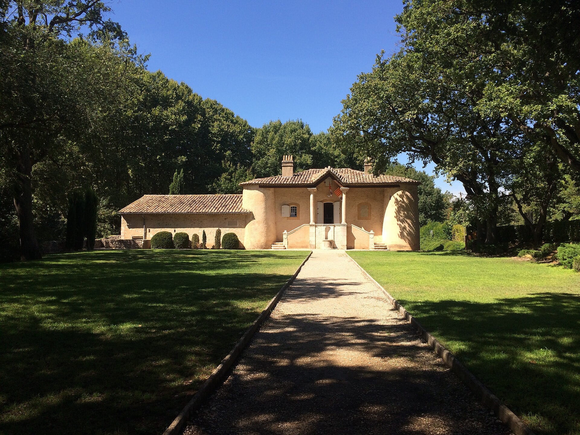 Pavillon de chasse provençal à un étage, façade claire percée de baies symétriques, précédé d’une allée rectiligne bordée d’arbres, à Gardanne.