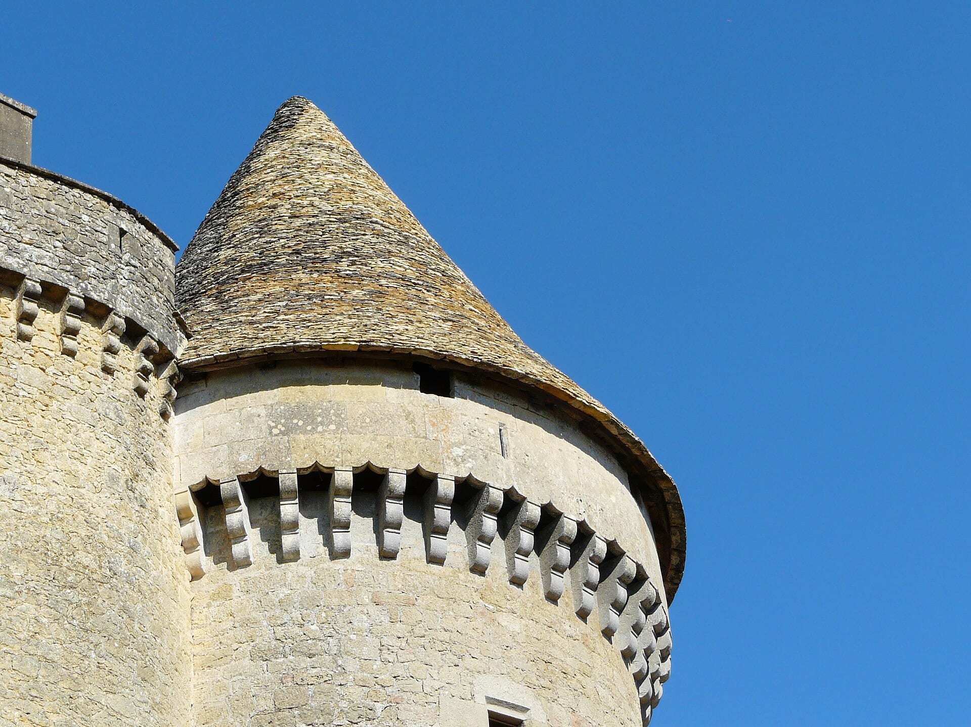 Grosse tour ronde à mâchicoulis coiffée d’un toit conique de lauzes, au château de Fénelon