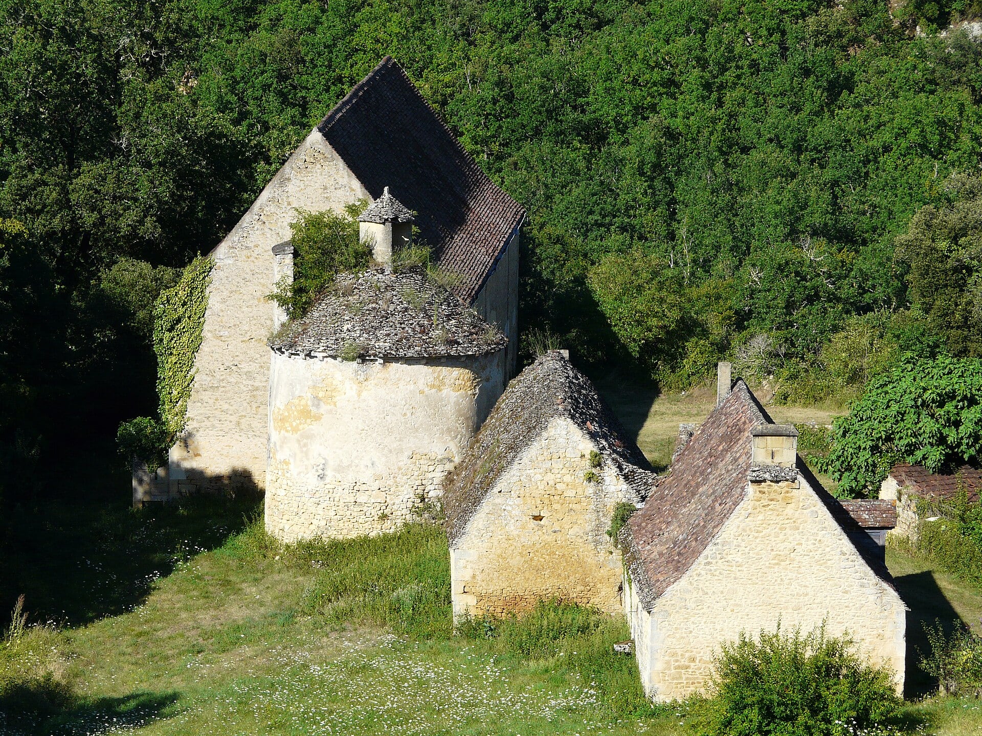 Deux maisons de pierre à toits de lauzes pentus, à flanc de coteau boisé