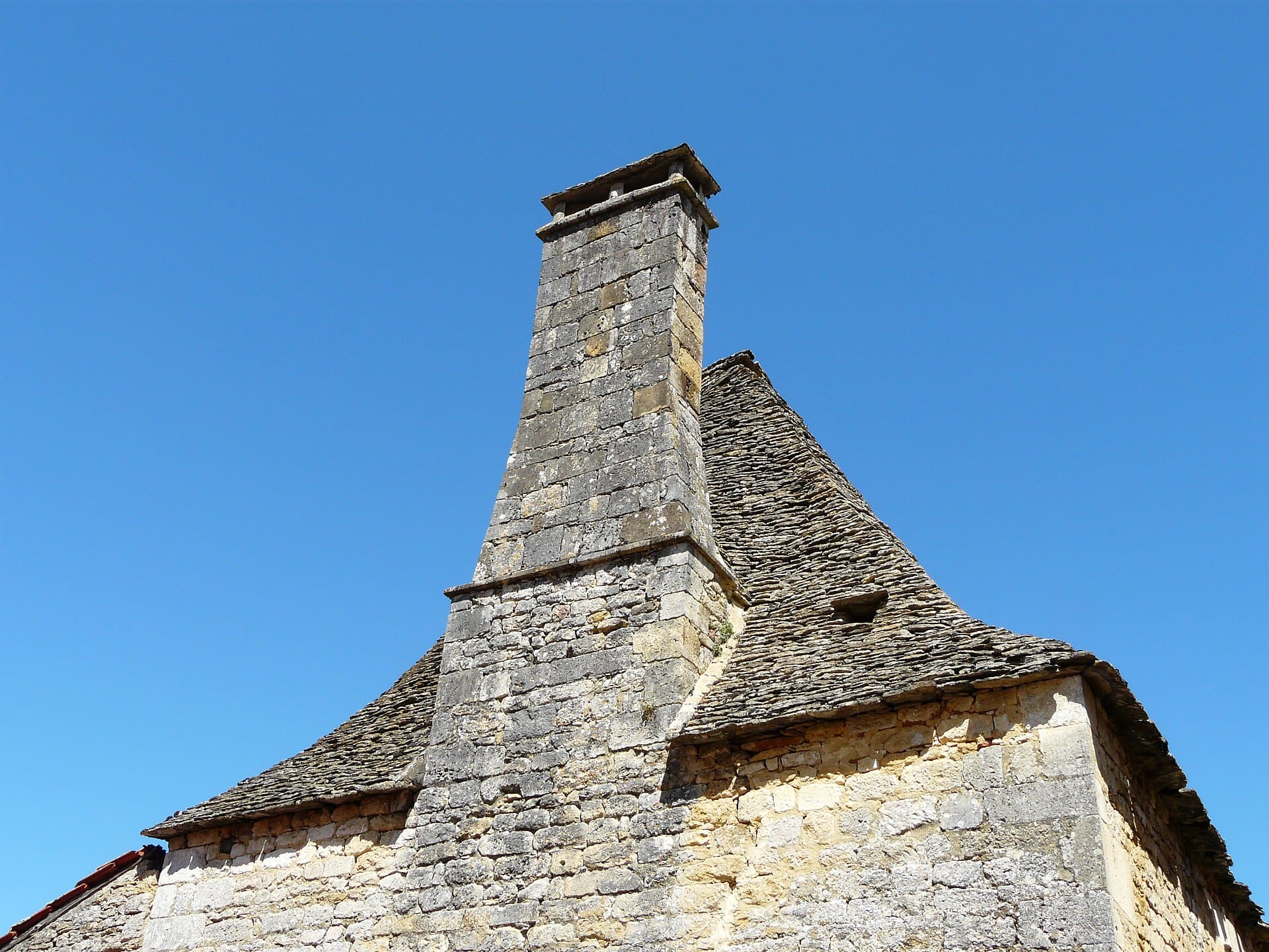 Angle d’un logis de pierre à toit de lauzes et haute souche de cheminée à Saint-Amand-de-Coly