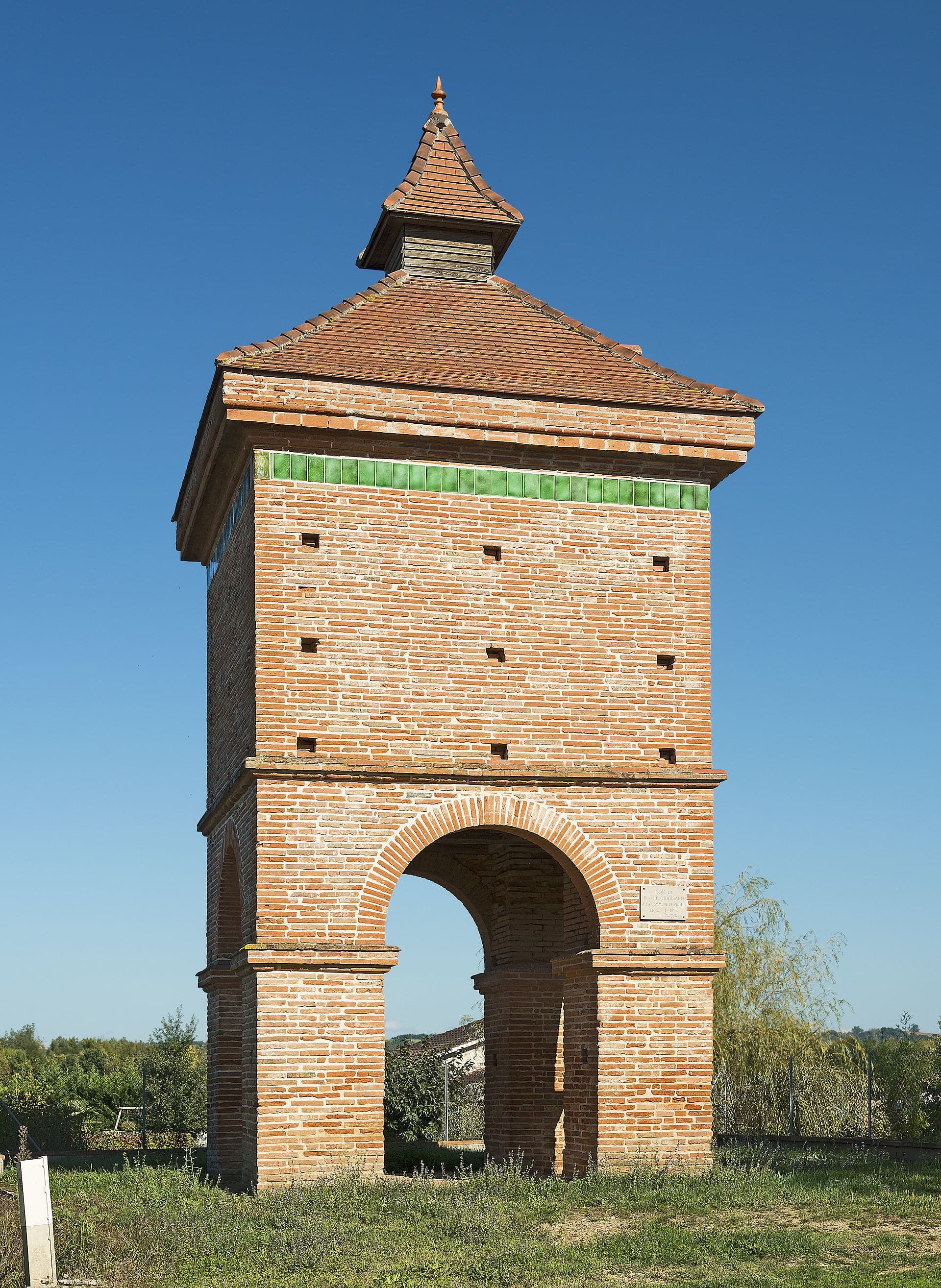 Le pigeonnier de la Mounette à Nohic (Tarn-et-Garonne), tour de brique rose dressée sur une arcade, coiffée d’un toit pyramidal à lanternon et soulignée d’un bandeau de tuiles vernissées vertes.