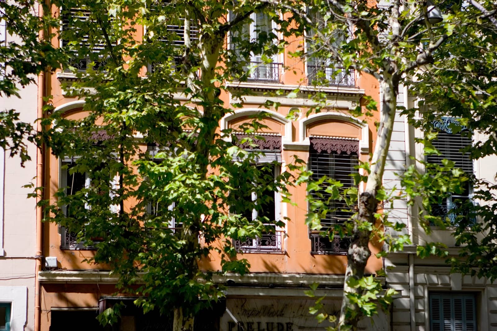 Haute façade ocre d’un immeuble de canuts sur les pentes de la Croix-Rousse à Lyon, percée de grandes fenêtres d’atelier