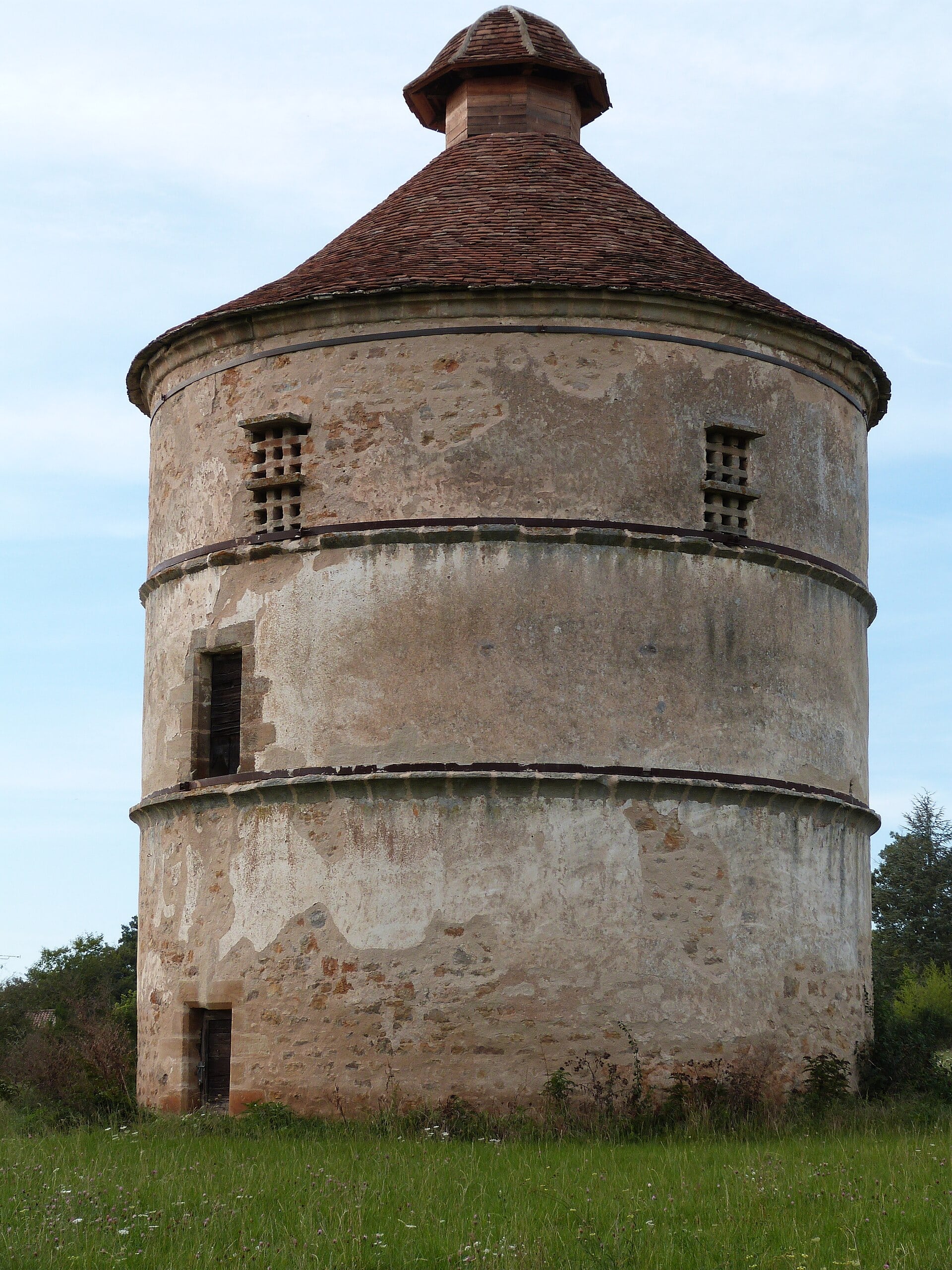 Grand pigeonnier-tour rond en pierre à toit conique, au château d’Assier, dans le Lot.