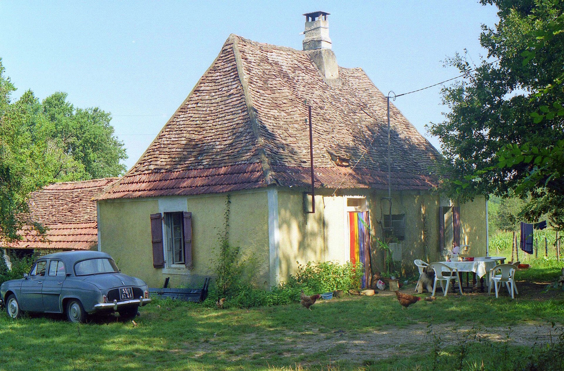Maison quercynoise basse en calcaire clair sous un toit de tuiles brunes, dans un jardin de campagne