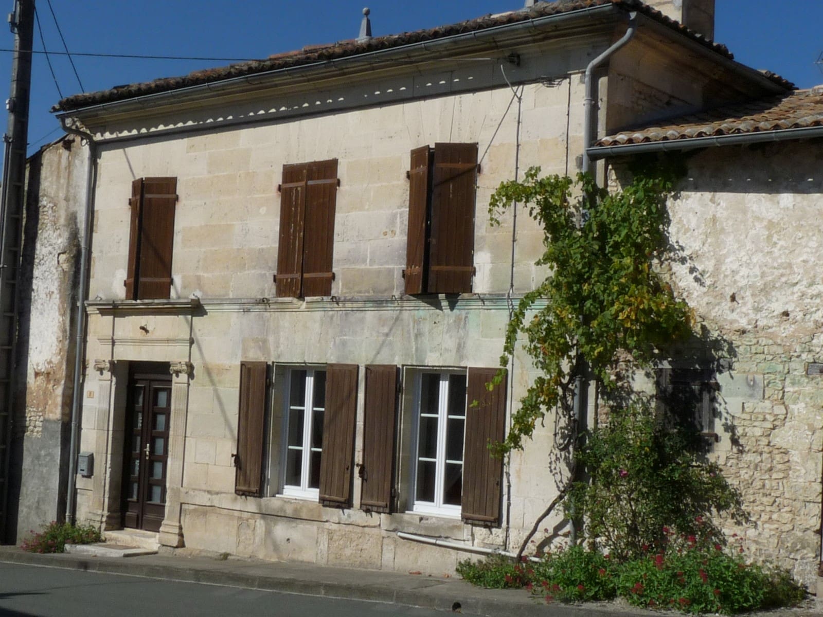 Façade de maison de bourg à Arthenac, en pierre de taille calcaire blonde, encadrement de porte mouluré à corniche, volets bruns