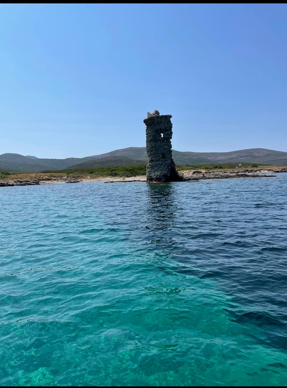 Tour de guet génoise ruinée, de plan carré, en pierre sombre, sur une pointe rocheuse du Cap Corse au bord d'une eau turquoise