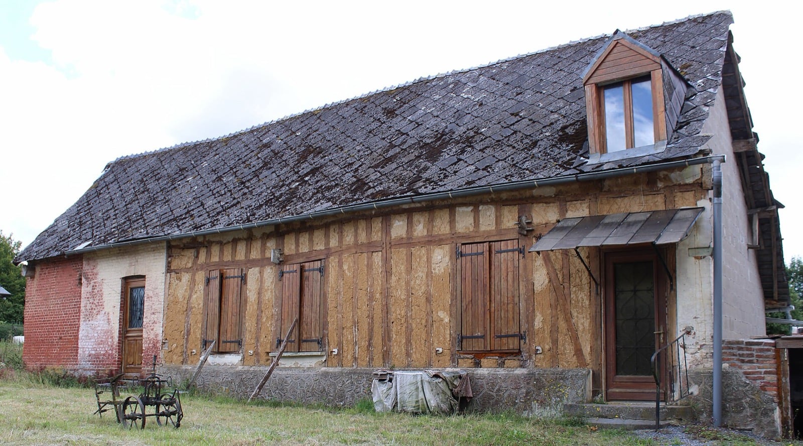 Longère dont le pan de bois laisse voir un remplissage de torchis ocre, sous un toit de tuiles plates à forte pente
