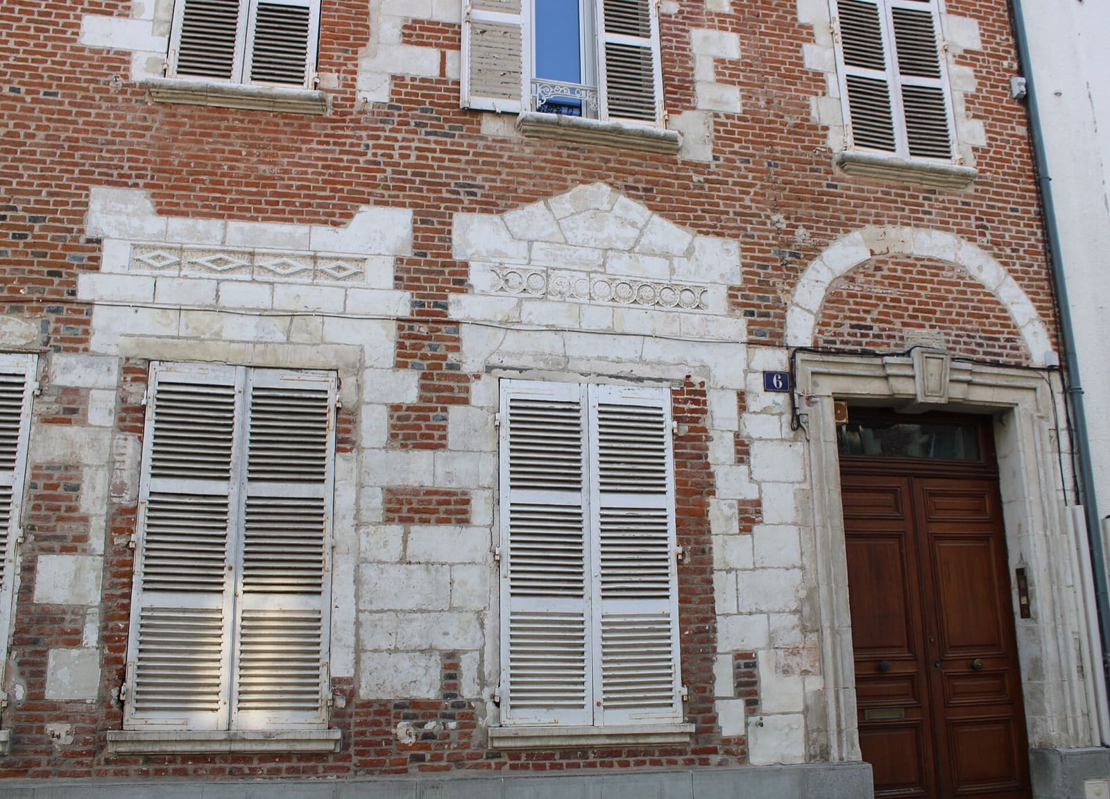 Façade de brique d’un ancien relais de poste à Marle : fenêtres et porte encadrées de pierre calcaire, large porte charretière cintrée à droite, numéro « 6 » apposé au mur.