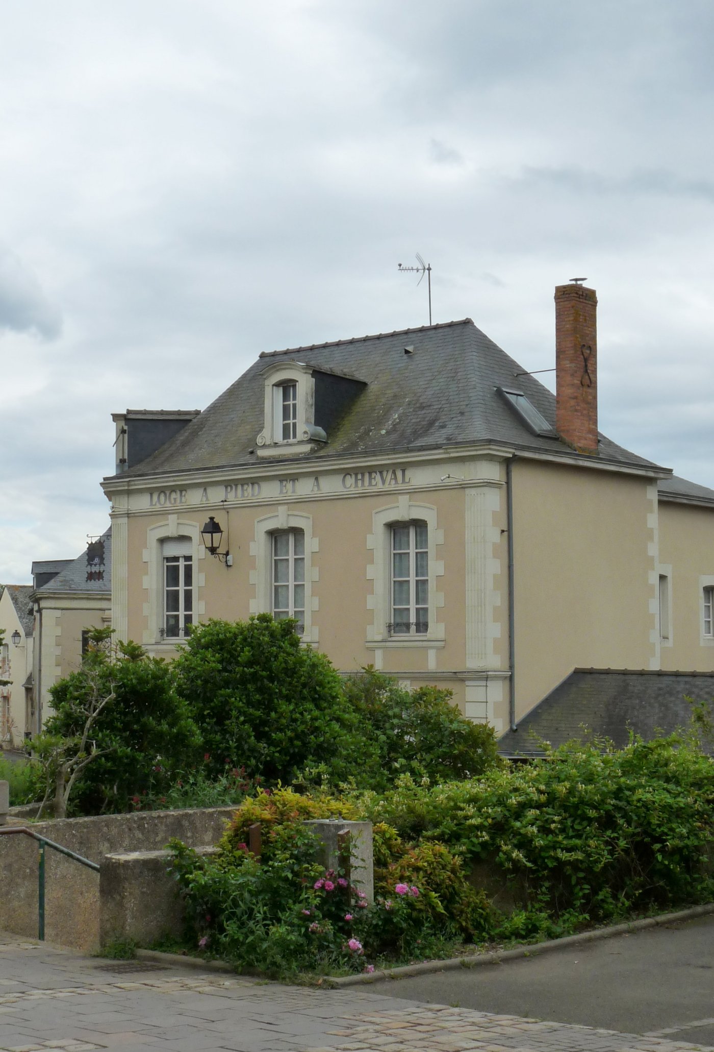 Façade classique d’un ancien relais de poste avec l’inscription gravée « Loge à pied et à cheval », lucarne et cheminées, à Saint-Denis-d’Anjou.