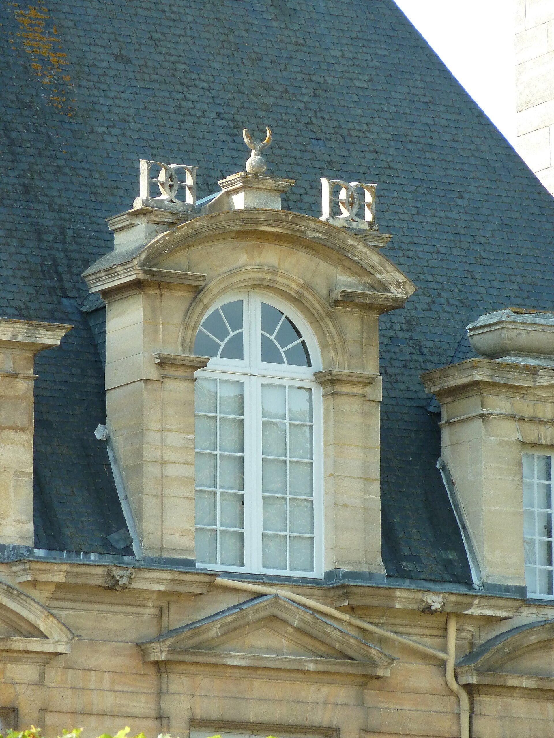 Lucarne du château d’Anet à fronton cintré, ornée du chiffre entrelacé de Diane de Poitiers et du croissant de lune, sur un haut comble d’ardoise