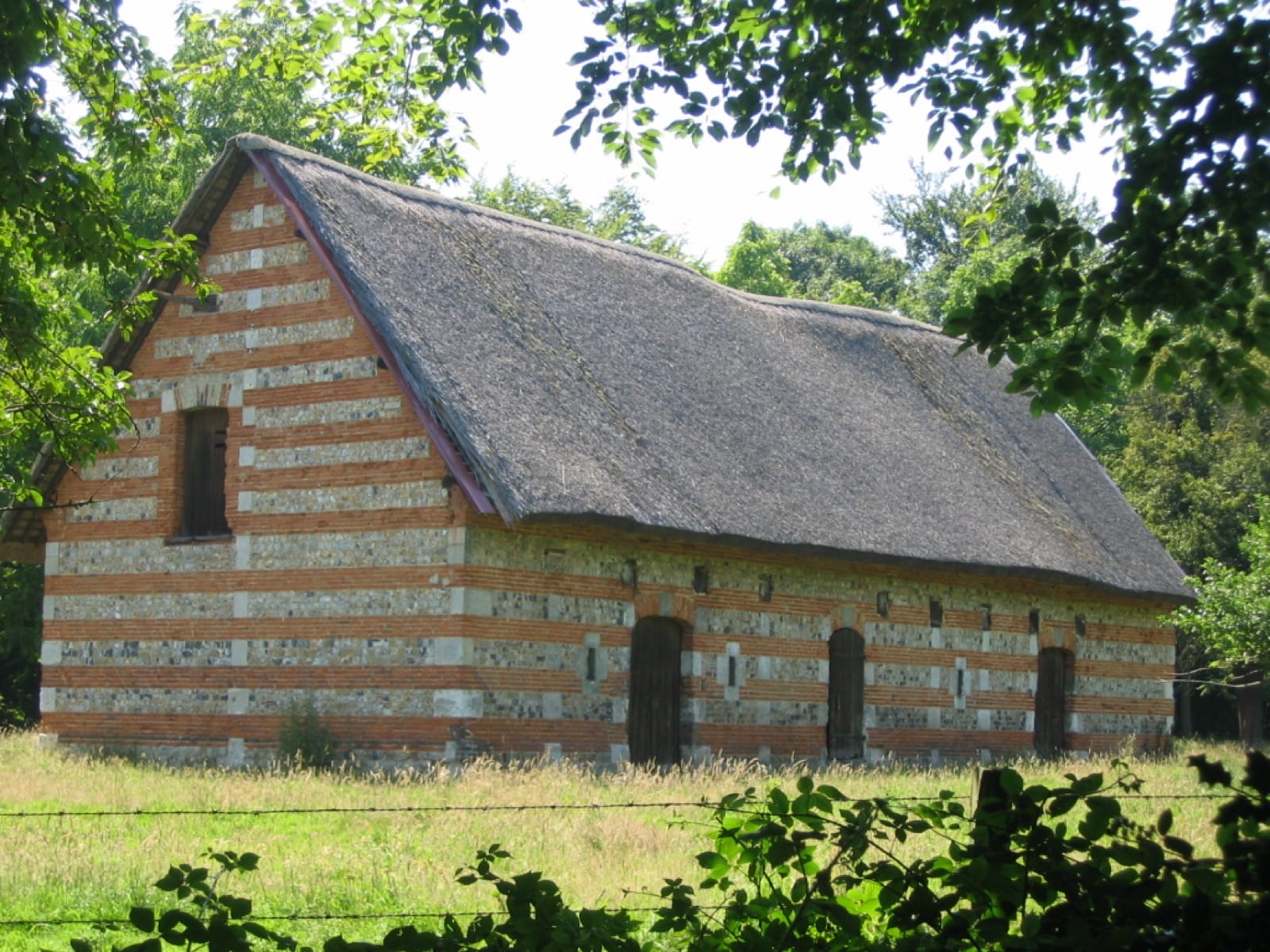 Bâtiment cauchois aux murs rayés de silex, de brique et de craie, sous un toit de chaume