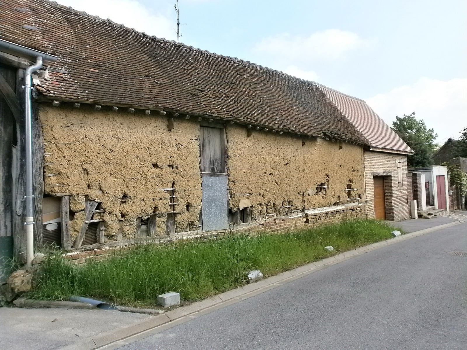 Long bâtiment agricole du Meux, dans l’Oise : large panneau de torchis ocre laissé nu entre les bois d’une ossature, sur soubassement de brique, sous un toit de tuiles