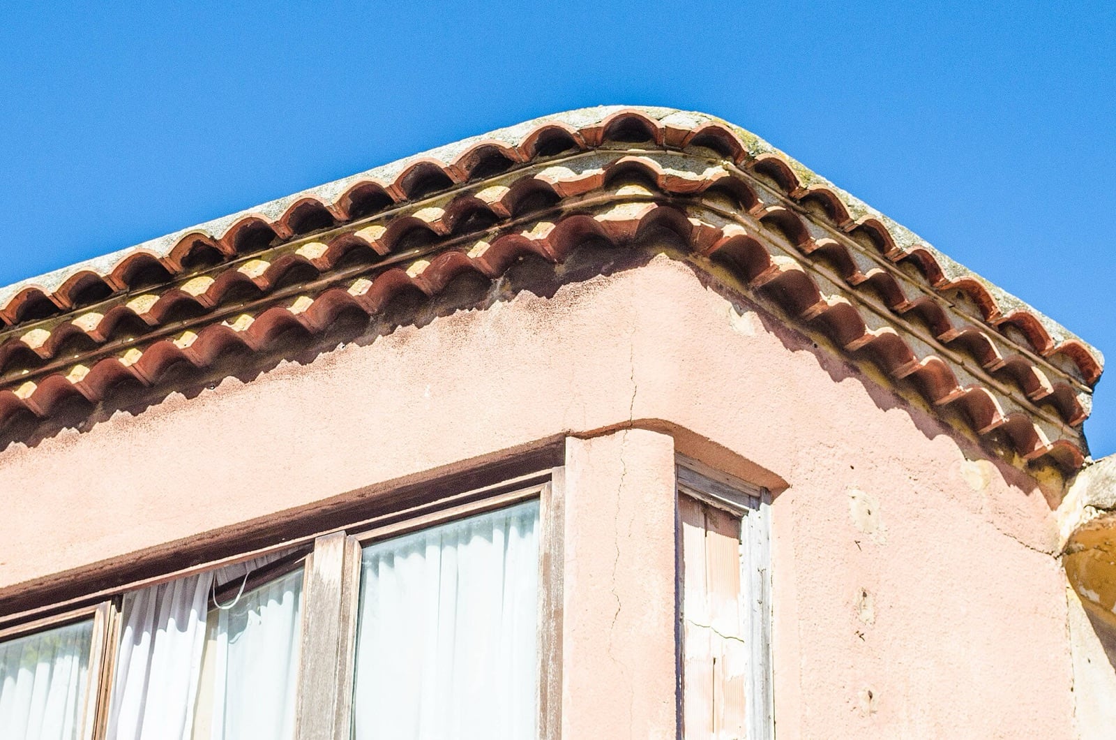 Génoise provençale, rangs de tuiles canal en encorbellement sous l’avant-toit d’une façade rose, ciel bleu