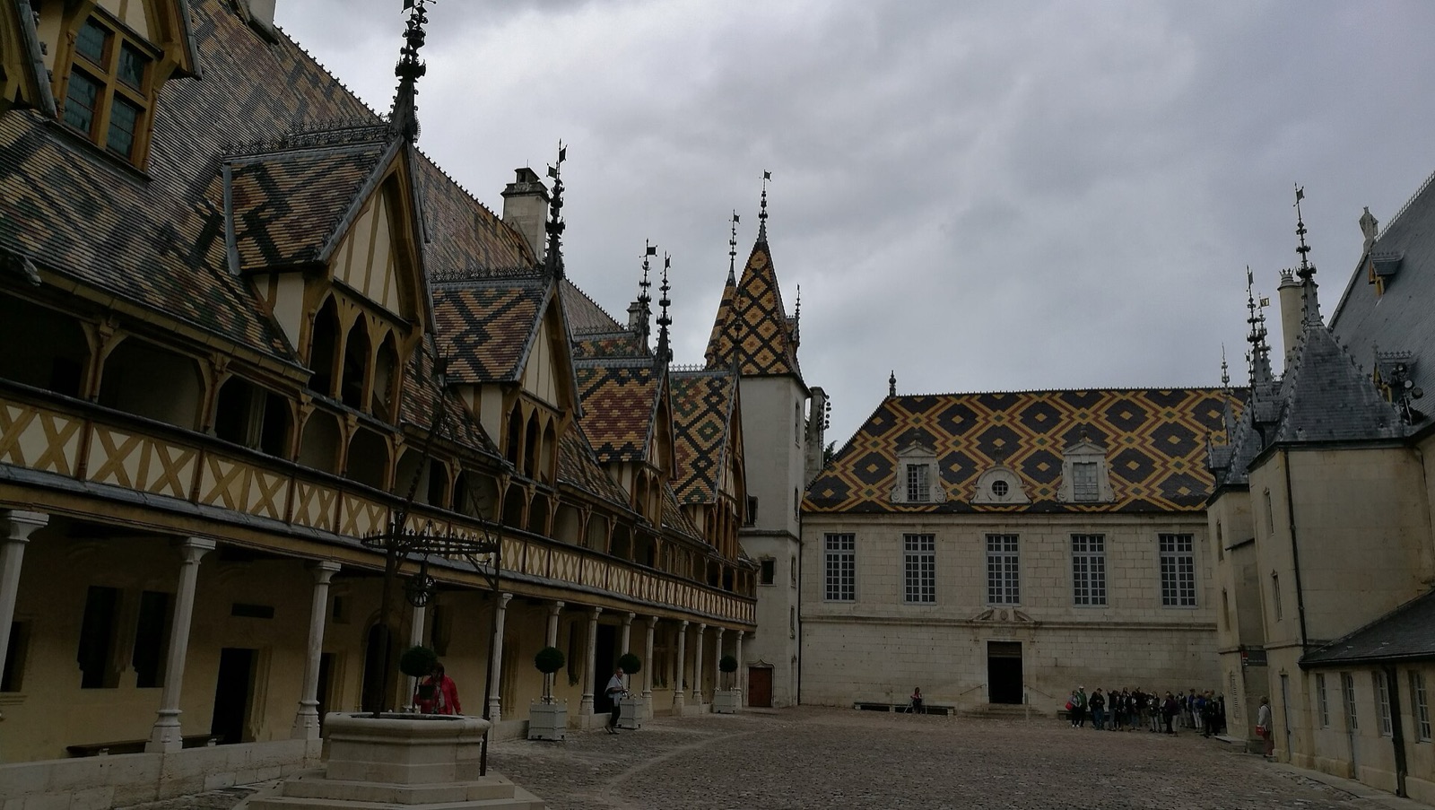 Cour intérieure de l’Hôtel-Dieu de Beaune cernée de ses toits de tuiles plates vernissées à losanges, galeries de bois et puits