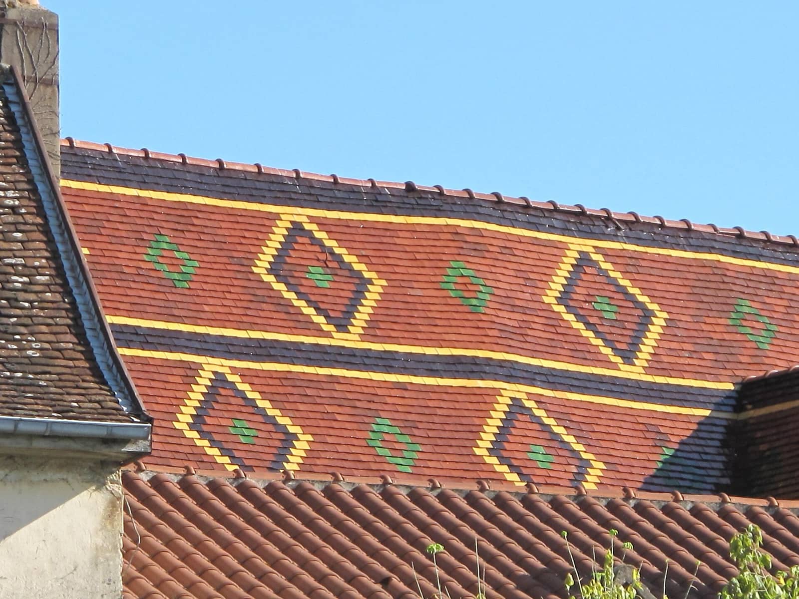Toit d’église bressane : champ de tuiles plates de terre cuite rousse et bandes vernissées à losanges jaunes, noirs et verts, à Louhans
