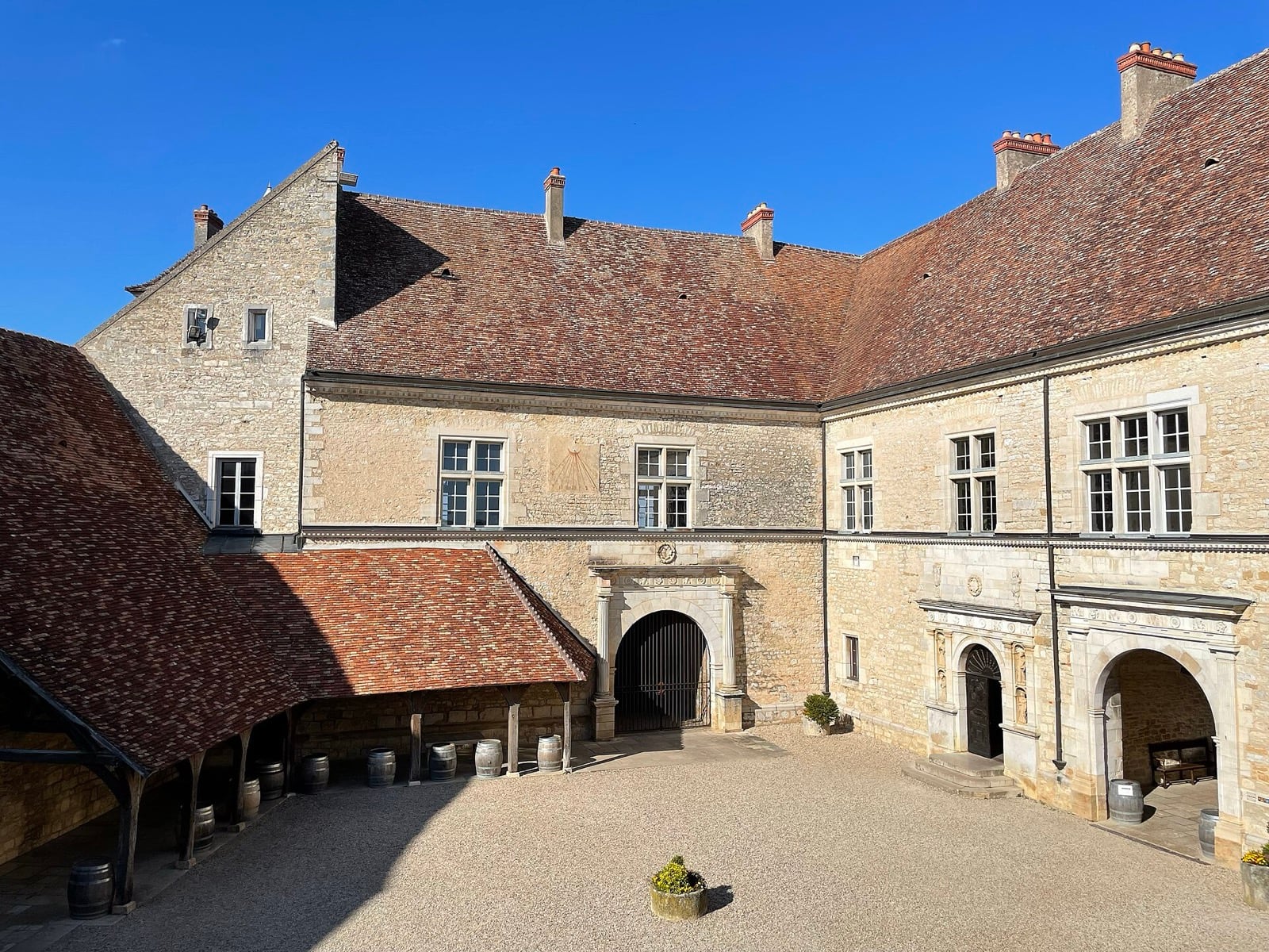 Cour intérieure du château du Clos de Vougeot : barriques rangées sous une arcade de pierre, portail voûté au fond