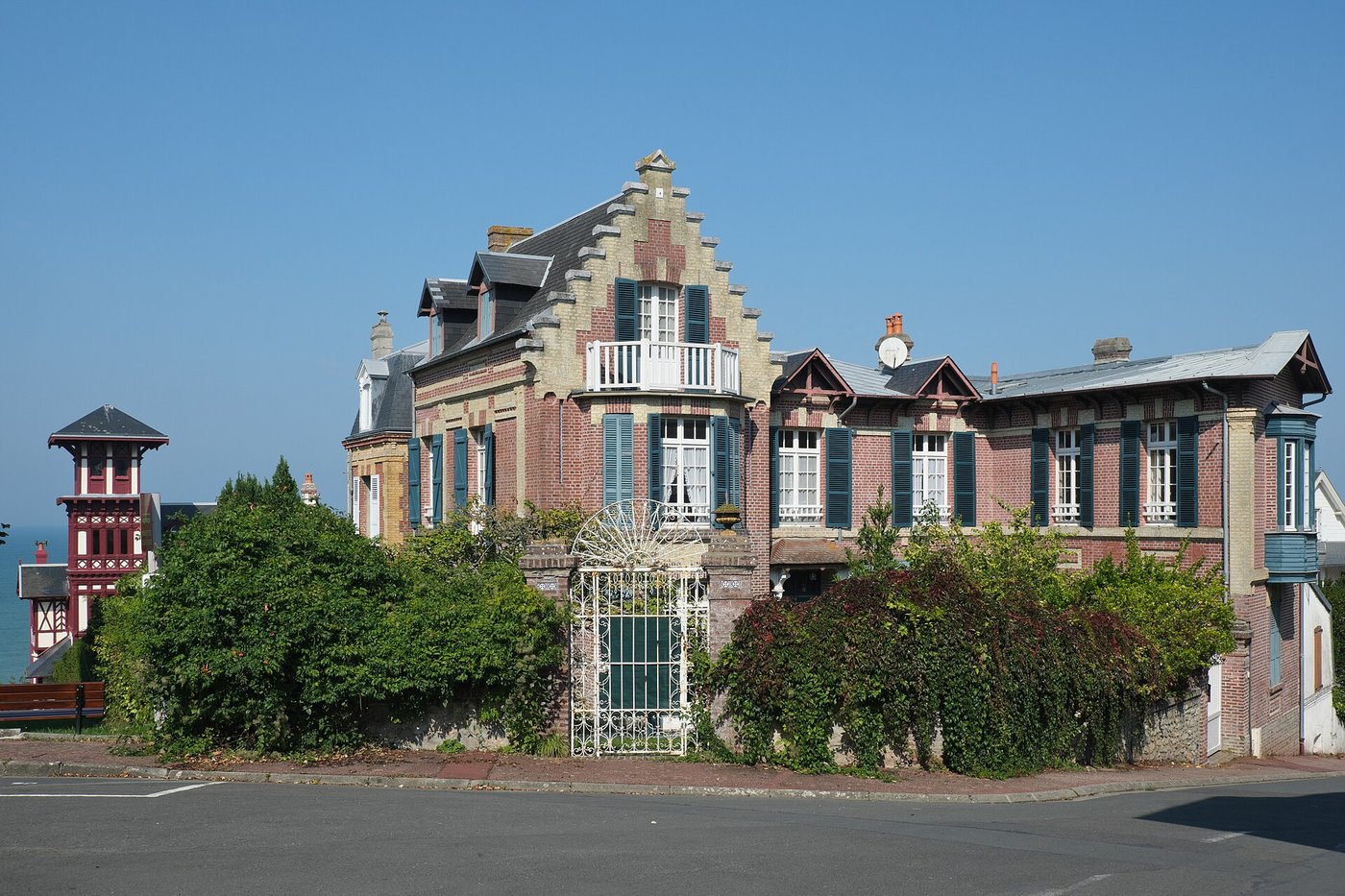 Villa balnéaire éclectique en brique polychrome, pignon à gradins et volets bleu-vert, avec une tourelle voisine à colombages visible en arrière-plan, à Villers-sur-Mer.