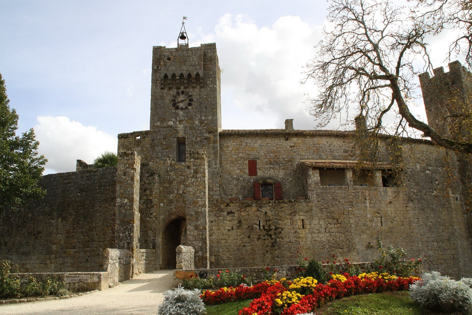 La porte fortifiée de Larressingle, dans le Gers : tour-porte à horloge percée d’un arc, courtine crénelée de part et d’autre