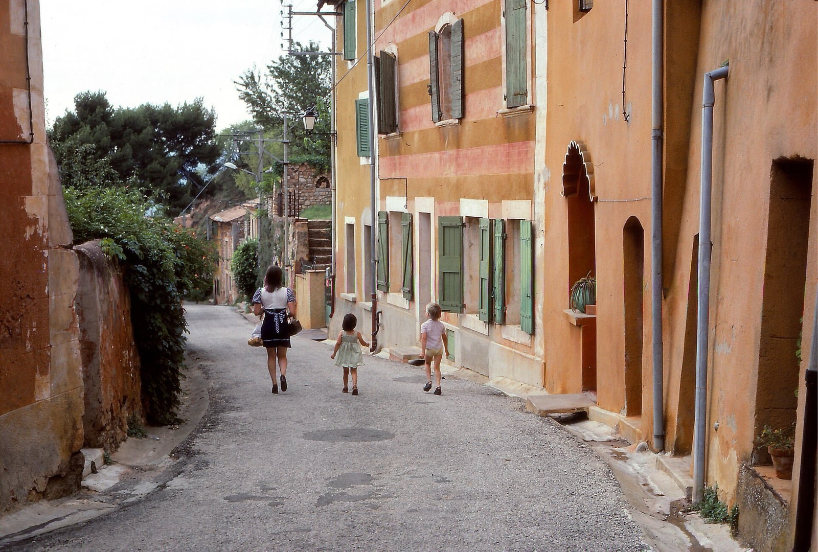 Rue étroite en montée à Roussillon, entre des façades ocre et rose