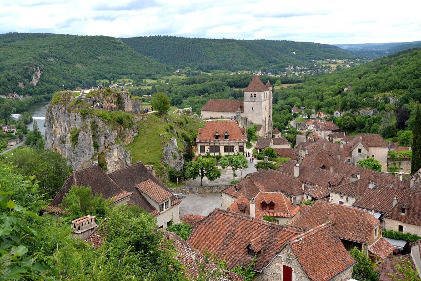 Saint-Cirq-Lapopie : toits de tuile brune et clocher au-dessus de la falaise calcaire et d’un rapide du Lot