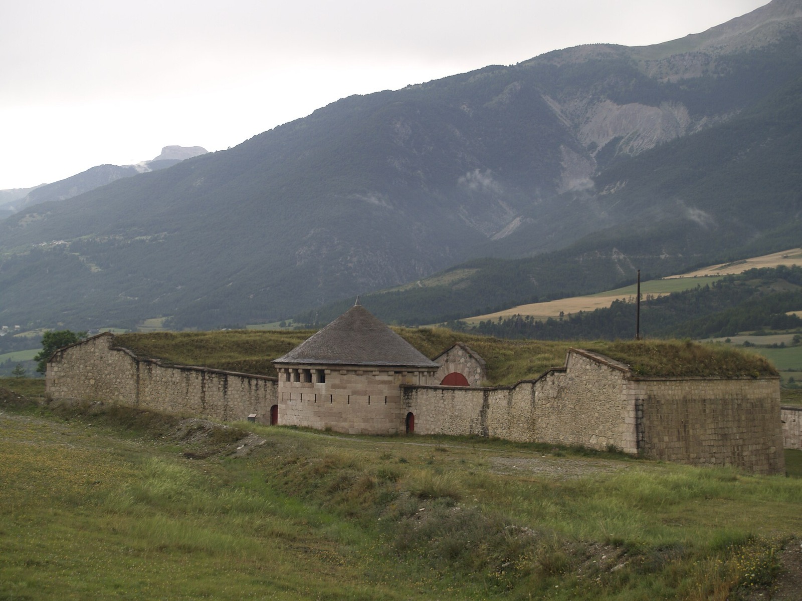 Ouvrage de fortification au fort de Mont-Dauphin : mur de pierre bas et épais coiffé d’un talus herbeux, tourelle de guet en encorbellement