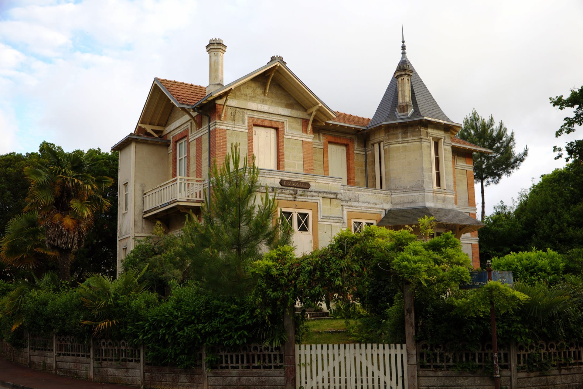Une villa de la ville d’hiver d’Arcachon nommée « Fragonard » : demeure éclectique de pierre et brique à tourelle d’ardoise pointue et balcon de bois, entourée de pins et de palmiers