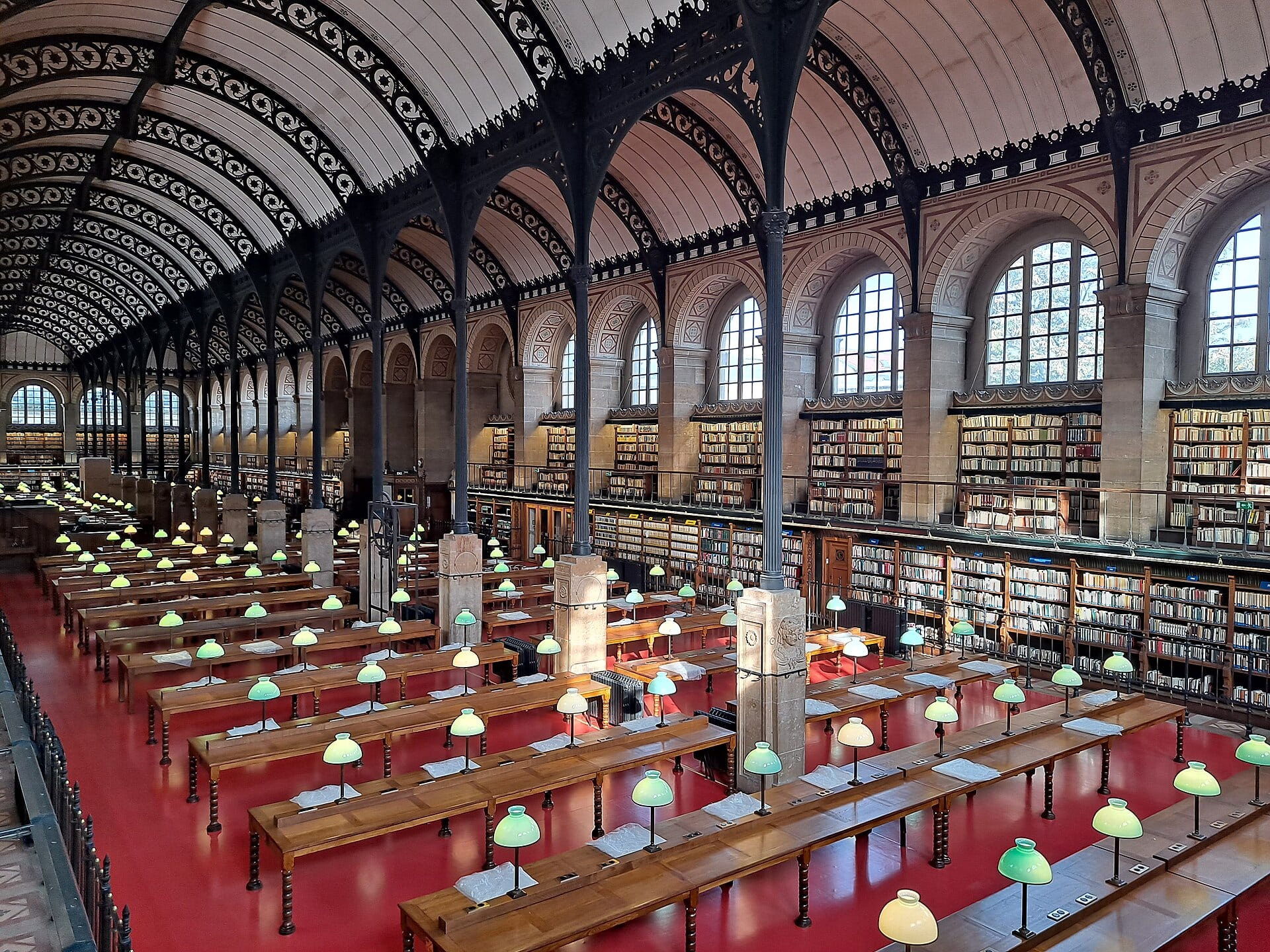 La salle de lecture de la bibliothèque Sainte-Geneviève (Henri Labrouste) : voûtes et colonnes de fonte ajourées, tables à lampes vertes, rayonnages sur deux niveaux